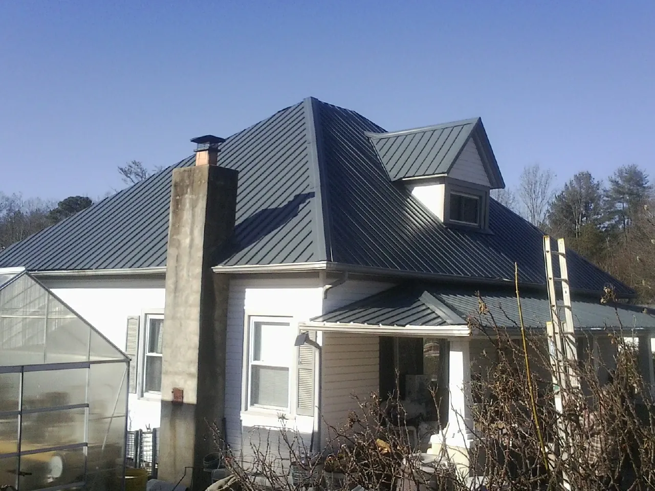 Dark blue standing seam metal roof on a white farmhouse with dormer — Slate & Tile Roof Repair by Roofing Brothers in Ashby