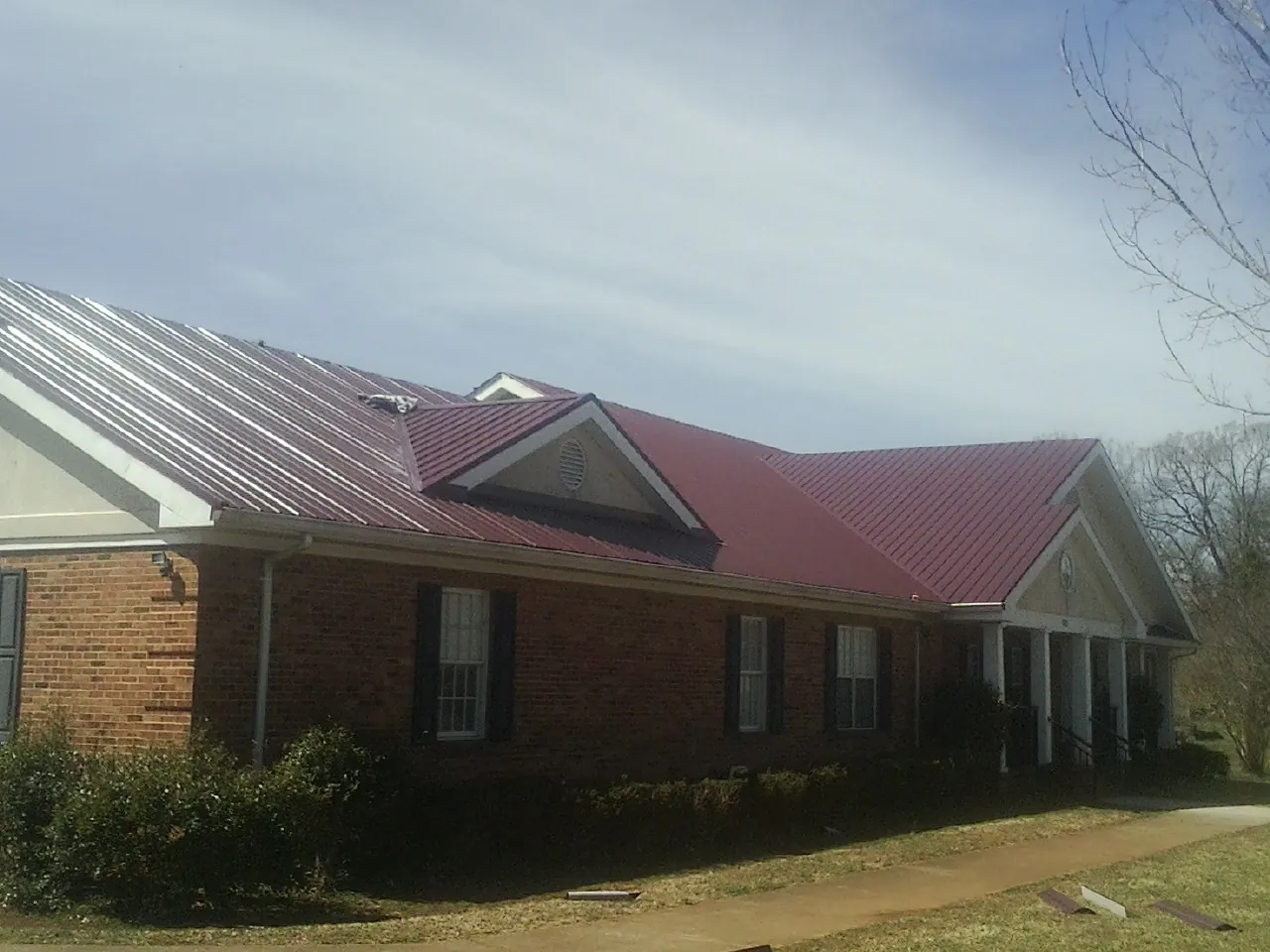 Red metal roof with gabled entries on a long brick building, from a Hail Damage Roof Repair job in Ashby