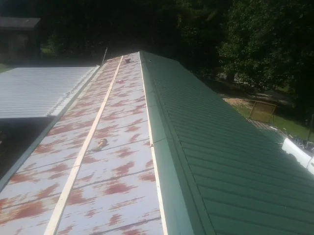 Old rusted panels beside newly installed green metal roofing — Wind Damage Roof Repair by Roofing Brothers in Ashby